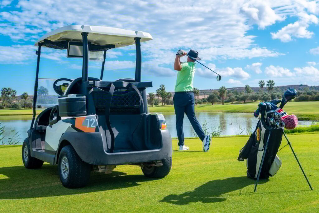 Man playing golf at golf club by a lake, hitting the ball next to the buggy car